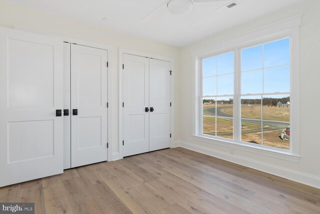 unfurnished bedroom featuring ceiling fan, light hardwood / wood-style floors, and two closets