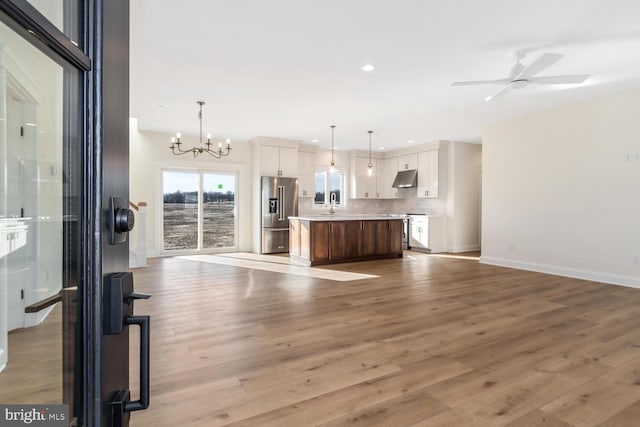 unfurnished living room featuring ceiling fan with notable chandelier, sink, and light hardwood / wood-style flooring