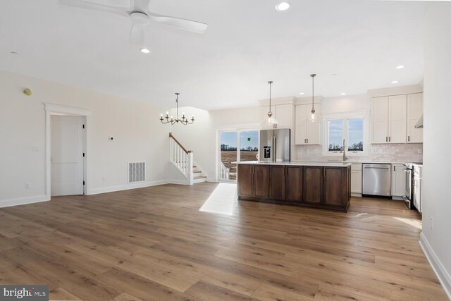 kitchen with a center island, stainless steel appliances, decorative light fixtures, decorative backsplash, and ceiling fan with notable chandelier