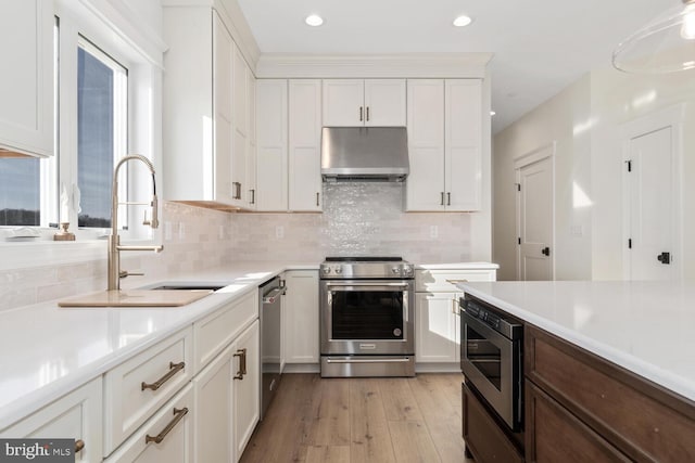 kitchen featuring white cabinetry, sink, stainless steel appliances, light hardwood / wood-style flooring, and exhaust hood