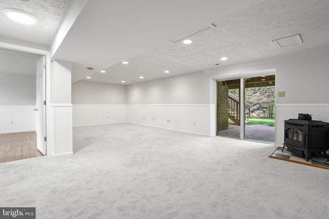 basement featuring light carpet, a textured ceiling, and a wood stove