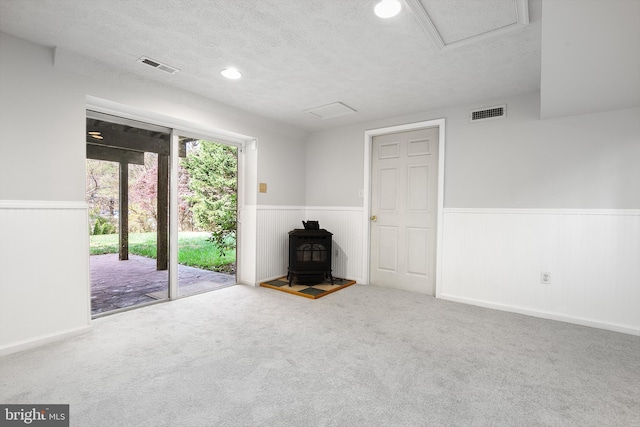 unfurnished living room with carpet flooring, a wood stove, and a textured ceiling