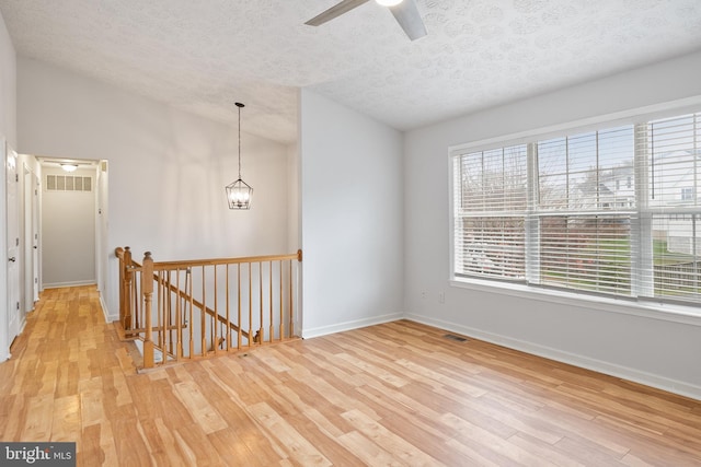 empty room featuring lofted ceiling, ceiling fan, light wood-type flooring, and a textured ceiling