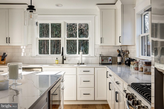 kitchen featuring light stone countertops, hanging light fixtures, sink, white cabinets, and stainless steel range with gas stovetop