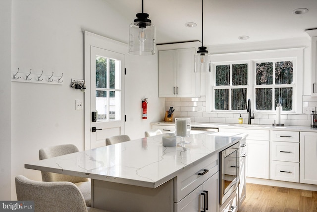 kitchen featuring a kitchen island, hanging light fixtures, a breakfast bar, white cabinets, and stainless steel microwave