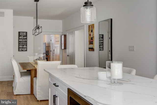 kitchen with hanging light fixtures, light stone countertops, white cabinetry, and light wood-type flooring