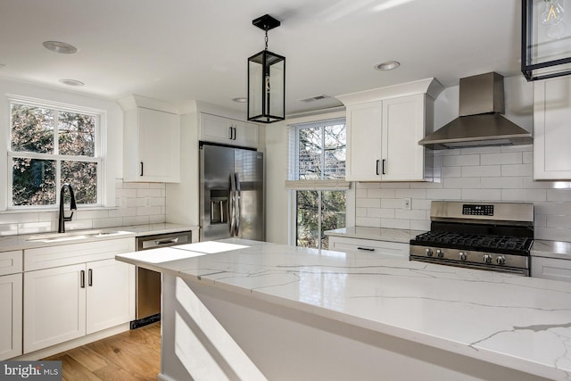 kitchen with white cabinetry, wall chimney range hood, appliances with stainless steel finishes, hanging light fixtures, and sink