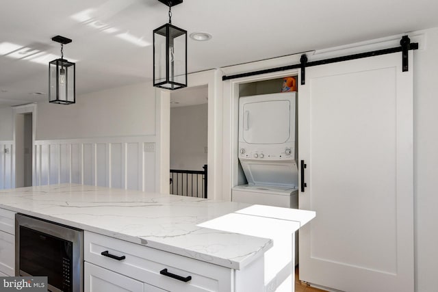 kitchen featuring pendant lighting, beverage cooler, stacked washer and dryer, and white cabinets