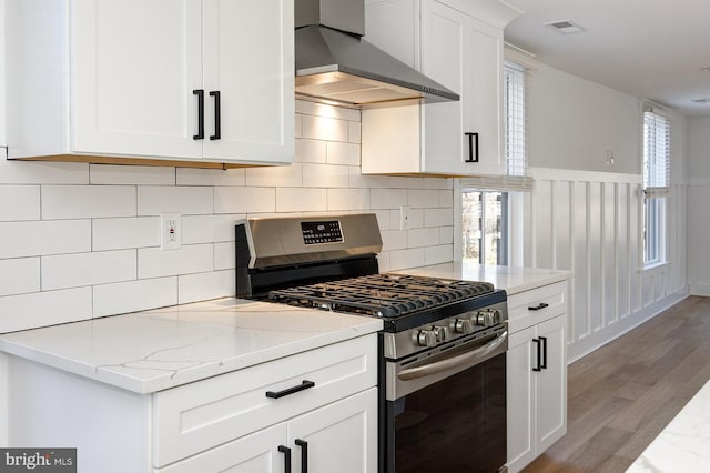 kitchen featuring white cabinetry, light stone counters, wall chimney exhaust hood, stainless steel gas range oven, and light wood-type flooring