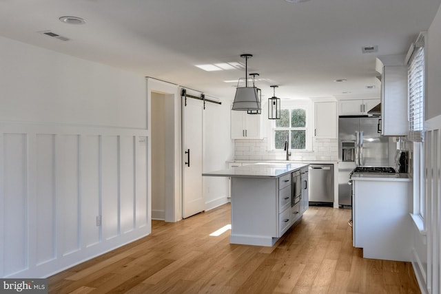 kitchen with a kitchen island, decorative light fixtures, a barn door, white cabinets, and dishwasher