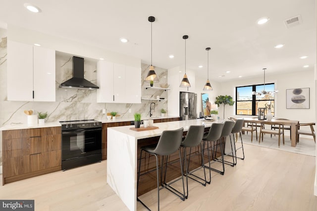 kitchen with white cabinets, light wood-type flooring, black range with electric cooktop, and wall chimney exhaust hood