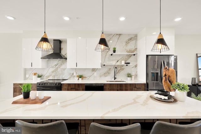 kitchen with black appliances, white cabinets, sink, wall chimney exhaust hood, and a breakfast bar area