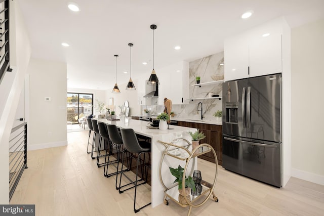 kitchen featuring sink, stainless steel fridge with ice dispenser, light hardwood / wood-style flooring, a center island with sink, and white cabinets