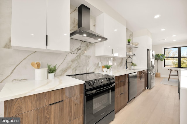 kitchen with appliances with stainless steel finishes, wall chimney exhaust hood, sink, light hardwood / wood-style floors, and white cabinetry