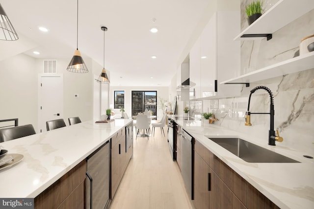 kitchen with light stone countertops, sink, stainless steel dishwasher, pendant lighting, and light hardwood / wood-style floors