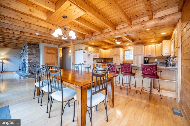 dining room with beamed ceiling, a fireplace, wood ceiling, a notable chandelier, and light wood-type flooring