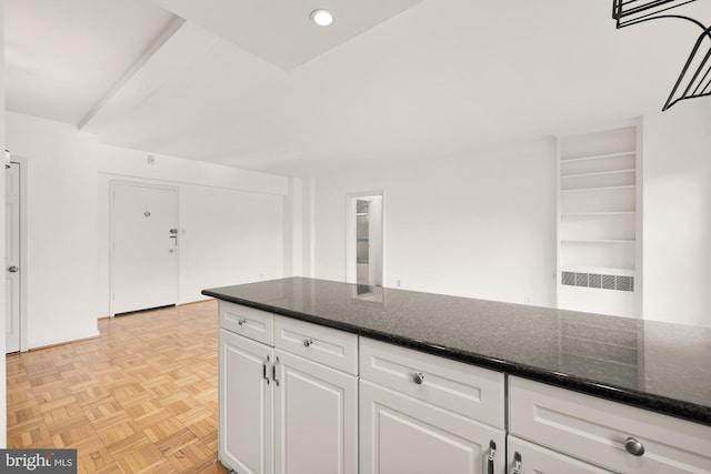 kitchen with white cabinetry, light parquet flooring, and dark stone counters