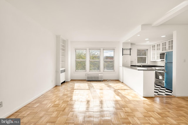 kitchen featuring light parquet flooring, white cabinetry, radiator heating unit, and stainless steel appliances