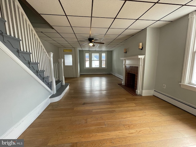 unfurnished living room with ceiling fan, light wood-type flooring, a baseboard heating unit, and a drop ceiling