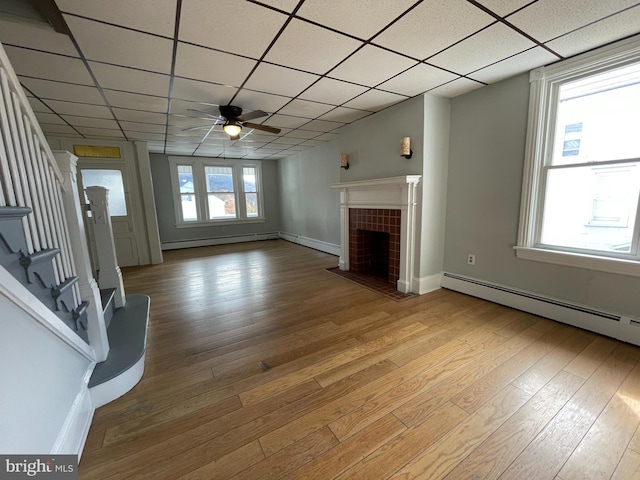 unfurnished living room with a fireplace, a paneled ceiling, light hardwood / wood-style flooring, and a baseboard heating unit