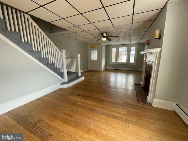 unfurnished living room with a drop ceiling, wood-type flooring, and a baseboard radiator