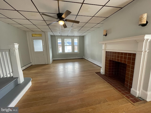 unfurnished living room with a baseboard radiator, a drop ceiling, wood-type flooring, and a fireplace