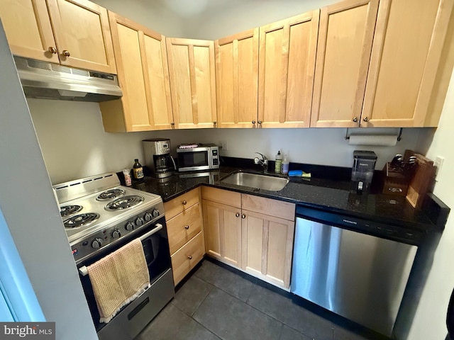 kitchen with dark stone counters, sink, dark tile patterned floors, appliances with stainless steel finishes, and light brown cabinetry