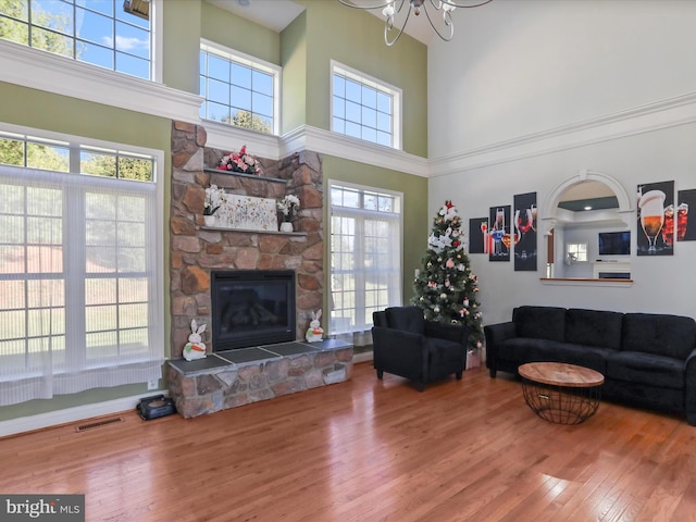 living room with a high ceiling, a stone fireplace, hardwood / wood-style floors, and a healthy amount of sunlight