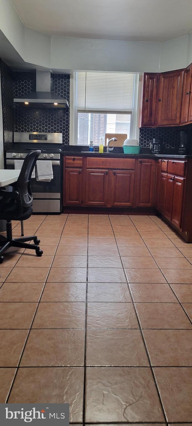 kitchen featuring sink, stainless steel range, light tile patterned flooring, wall chimney range hood, and backsplash