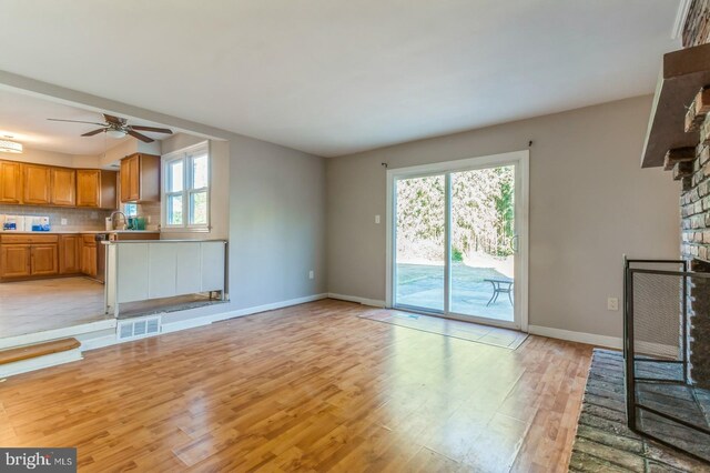 unfurnished living room featuring a fireplace, light hardwood / wood-style flooring, ceiling fan, and sink