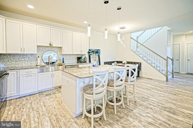 kitchen featuring pendant lighting, a center island, decorative backsplash, white cabinetry, and light wood-type flooring