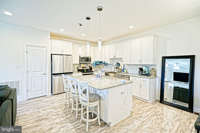 kitchen with light hardwood / wood-style flooring, hanging light fixtures, backsplash, white cabinetry, and appliances with stainless steel finishes