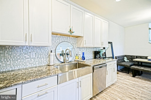 kitchen featuring white cabinetry, light stone countertops, sink, stainless steel dishwasher, and light hardwood / wood-style flooring