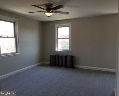 unfurnished room with carpet flooring, radiator, a healthy amount of sunlight, and ceiling fan