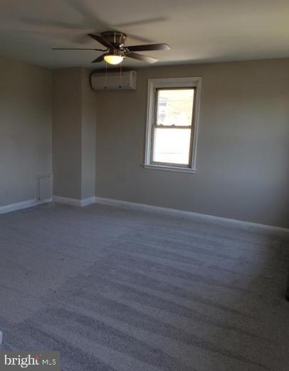 spare room featuring a wall unit AC, ceiling fan, and carpet flooring