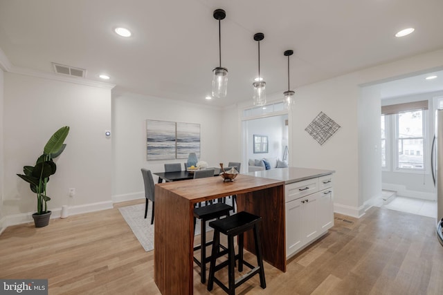 kitchen featuring pendant lighting, a center island, white cabinets, crown molding, and light hardwood / wood-style flooring