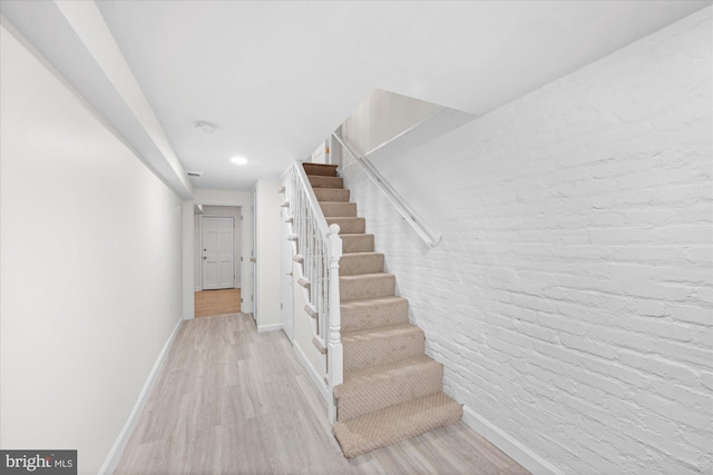 staircase with hardwood / wood-style floors and brick wall