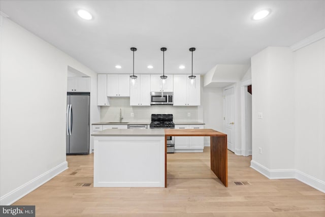 kitchen featuring white cabinets, appliances with stainless steel finishes, light hardwood / wood-style floors, and hanging light fixtures