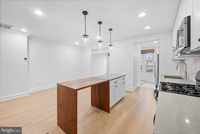 kitchen with sink, appliances with stainless steel finishes, pendant lighting, white cabinets, and light wood-type flooring