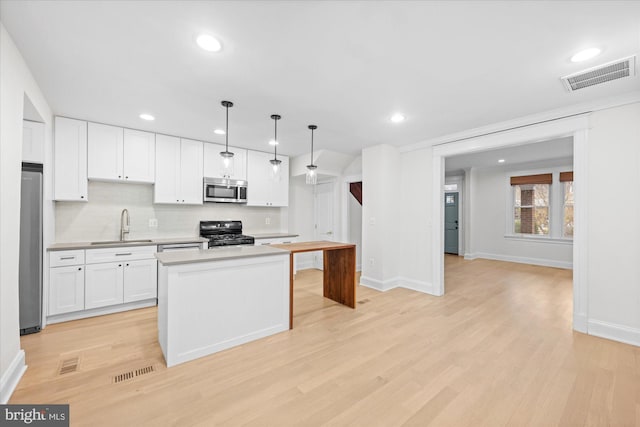 kitchen with hanging light fixtures, white cabinets, stainless steel appliances, and light wood-type flooring