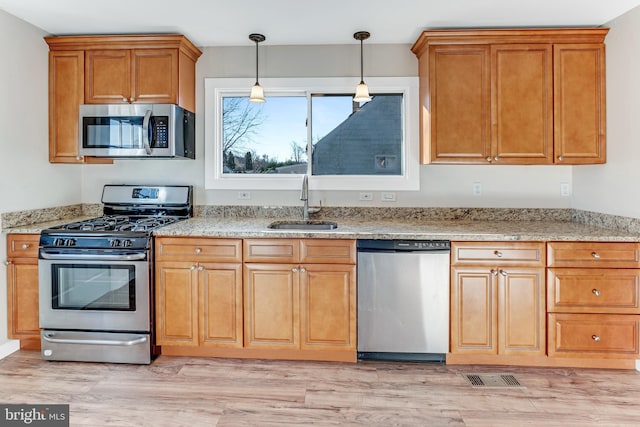 kitchen featuring sink, hanging light fixtures, light hardwood / wood-style flooring, light stone counters, and stainless steel appliances