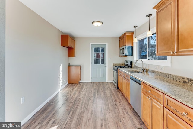 kitchen featuring sink, light stone counters, decorative light fixtures, appliances with stainless steel finishes, and hardwood / wood-style flooring