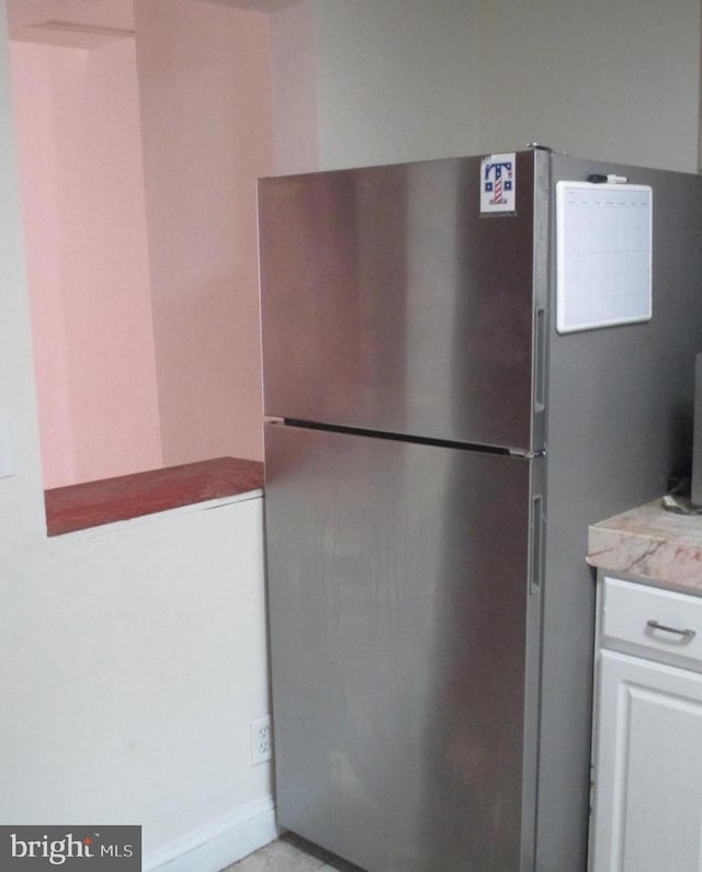 kitchen with stainless steel fridge, white cabinets, and light stone countertops