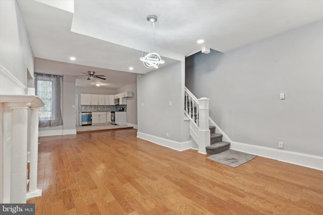 unfurnished living room with ceiling fan with notable chandelier and light hardwood / wood-style flooring