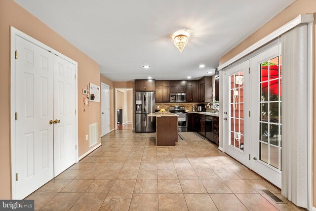 kitchen with stainless steel appliances, sink, backsplash, dark brown cabinets, and a center island