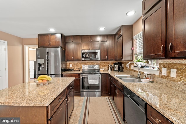 kitchen featuring stainless steel appliances, sink, light stone countertops, a center island, and decorative backsplash