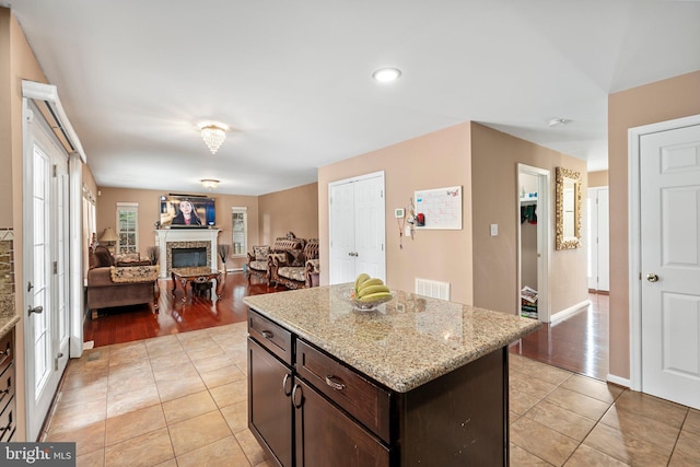 kitchen featuring light stone counters, a fireplace, light wood-type flooring, dark brown cabinets, and a center island