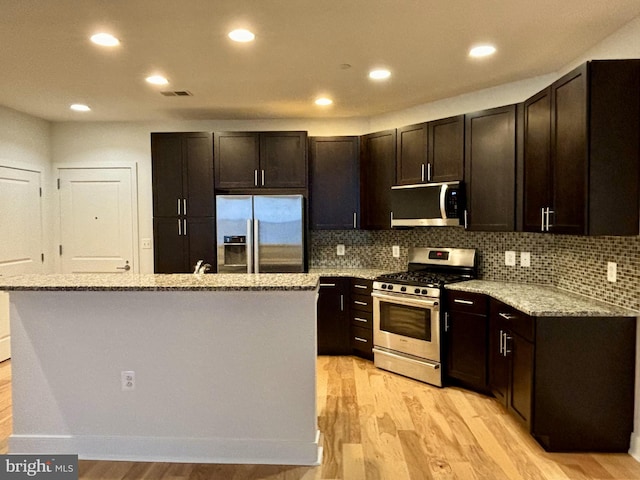 kitchen with stainless steel appliances, dark brown cabinetry, light stone countertops, light hardwood / wood-style floors, and a center island