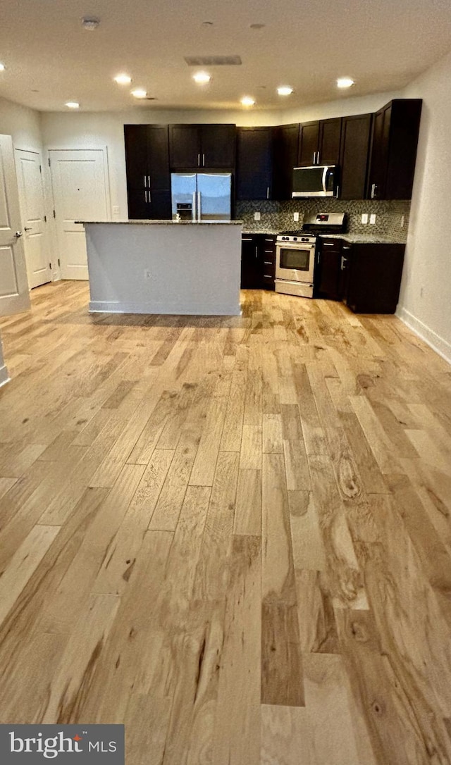 kitchen with decorative backsplash, appliances with stainless steel finishes, light hardwood / wood-style floors, and a kitchen island