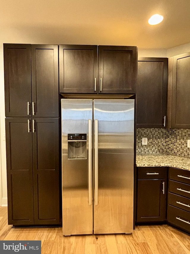 kitchen featuring dark brown cabinetry, stainless steel fridge, light hardwood / wood-style flooring, and light stone counters